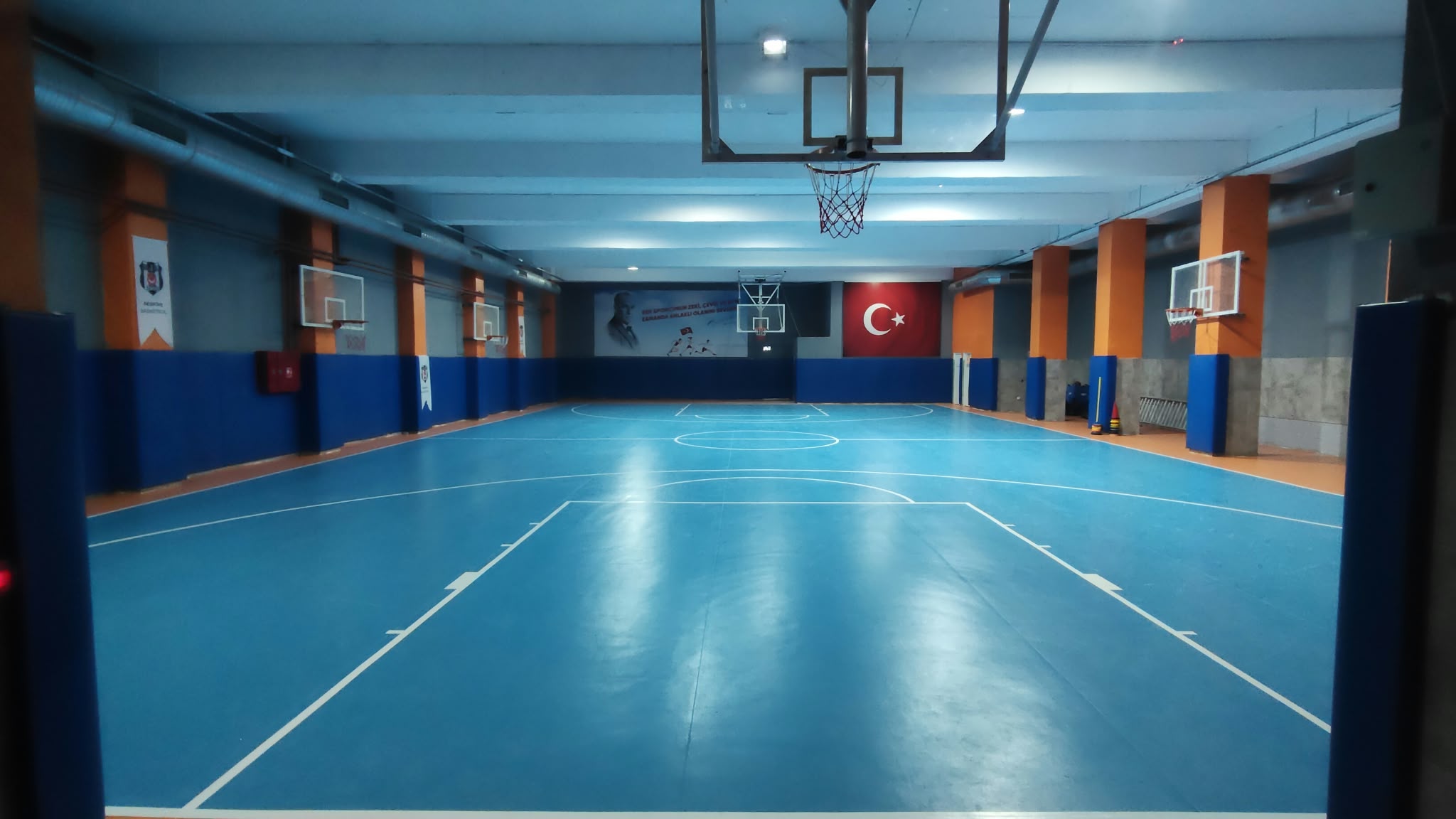 Mavi PVC spor zemini ve basketbol potalarının bulunduğu kapalı spor salonu